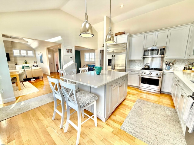 kitchen featuring light wood-type flooring, a kitchen island, a kitchen breakfast bar, decorative light fixtures, and high end appliances