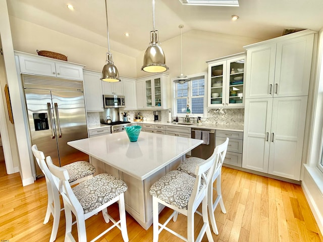 kitchen with lofted ceiling, a breakfast bar area, high quality appliances, hanging light fixtures, and a center island