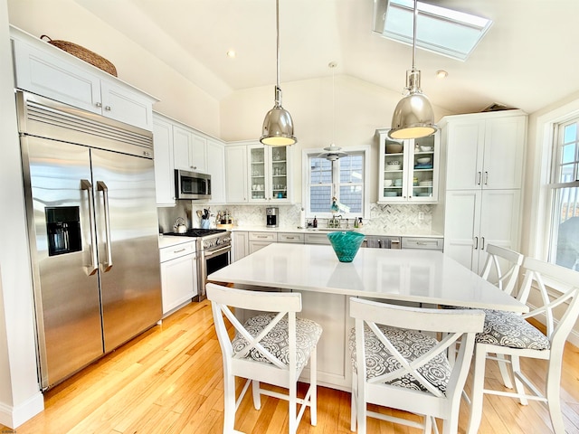 kitchen with a kitchen island, high end appliances, a kitchen bar, decorative light fixtures, and light wood-type flooring