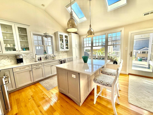 kitchen with tasteful backsplash, a center island, light hardwood / wood-style floors, vaulted ceiling with skylight, and pendant lighting