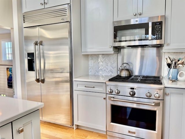 kitchen with high quality appliances, white cabinets, light hardwood / wood-style floors, and tasteful backsplash