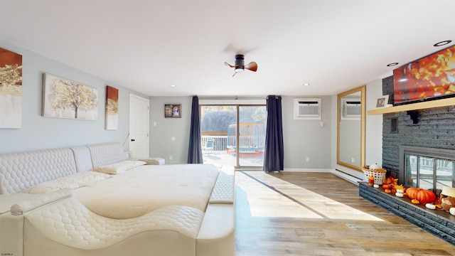 bedroom with a wall mounted AC, a stone fireplace, access to outside, and wood-type flooring