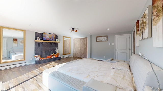 bedroom featuring wood-type flooring, a baseboard radiator, and a brick fireplace