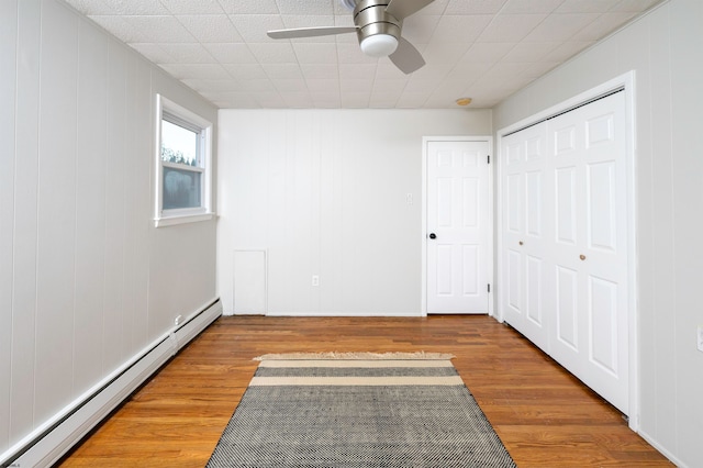 unfurnished bedroom featuring baseboard heating, hardwood / wood-style floors, and ceiling fan