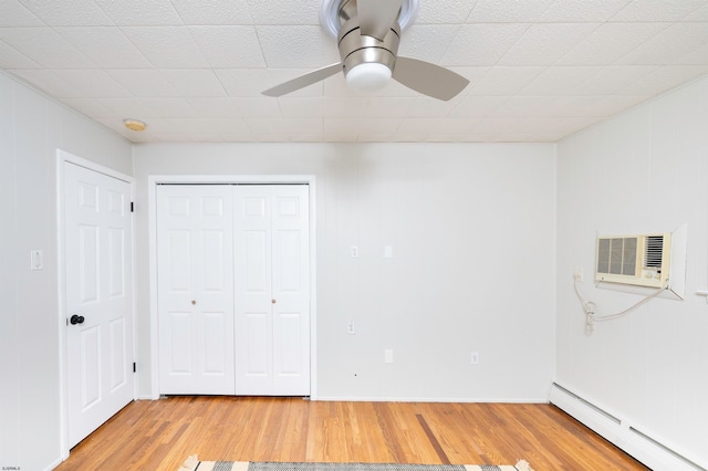 unfurnished bedroom featuring a wall unit AC, hardwood / wood-style flooring, a closet, a baseboard heating unit, and ceiling fan