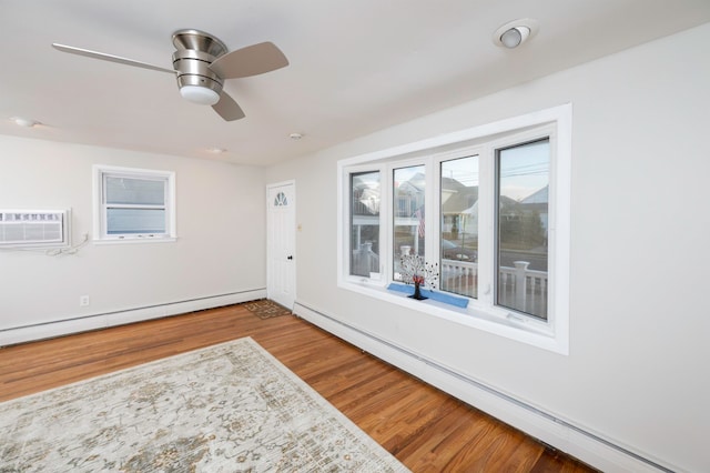 empty room with a wall mounted AC, wood-type flooring, a baseboard radiator, and ceiling fan