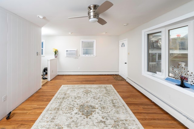 interior space featuring light hardwood / wood-style flooring, an AC wall unit, a baseboard radiator, and ceiling fan