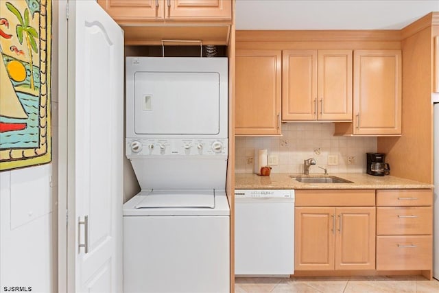 laundry area featuring stacked washing maching and dryer, light tile patterned flooring, and sink