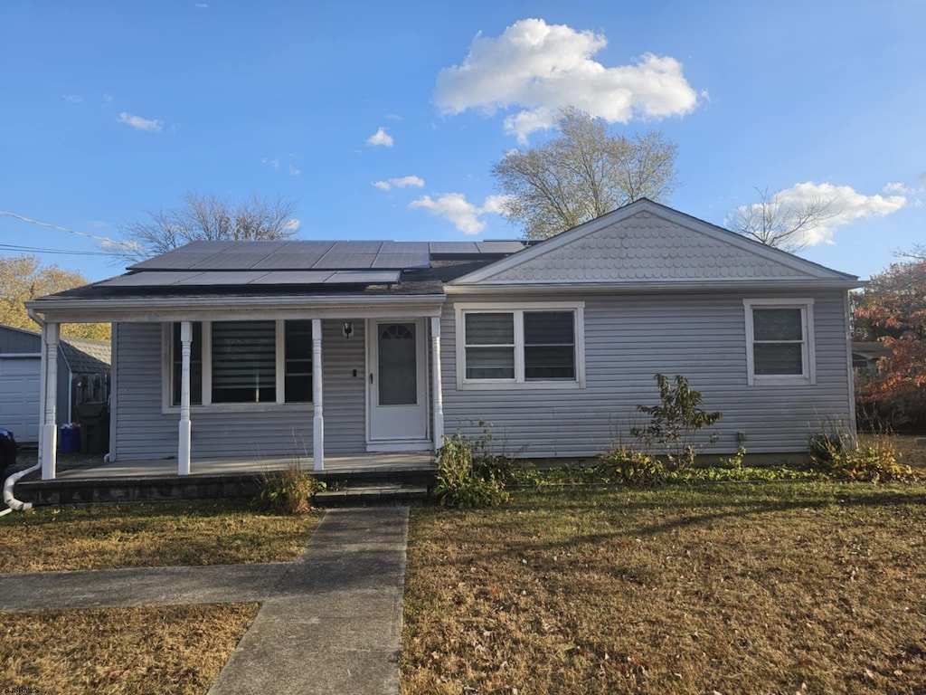 view of front of home with a porch, solar panels, and a front yard