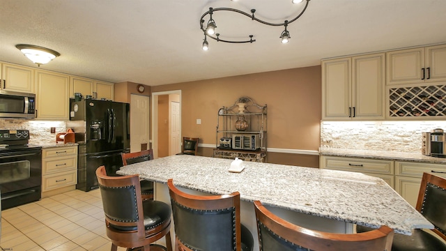 kitchen with light stone counters, black appliances, a kitchen bar, and cream cabinetry