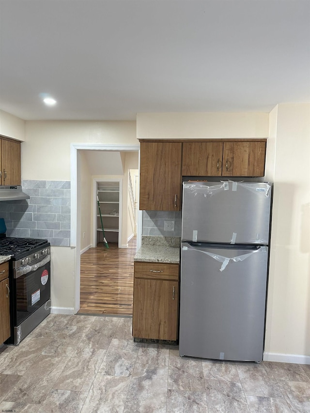 kitchen featuring light hardwood / wood-style floors, appliances with stainless steel finishes, light stone countertops, backsplash, and range hood