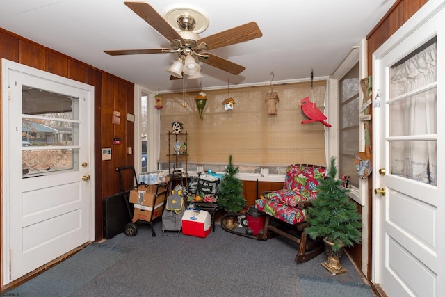 misc room featuring ceiling fan, wood walls, carpet flooring, and ornamental molding