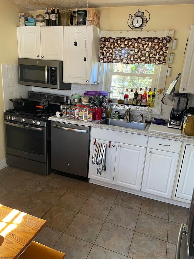 kitchen featuring stainless steel appliances, white cabinets, sink, tasteful backsplash, and dark tile patterned floors