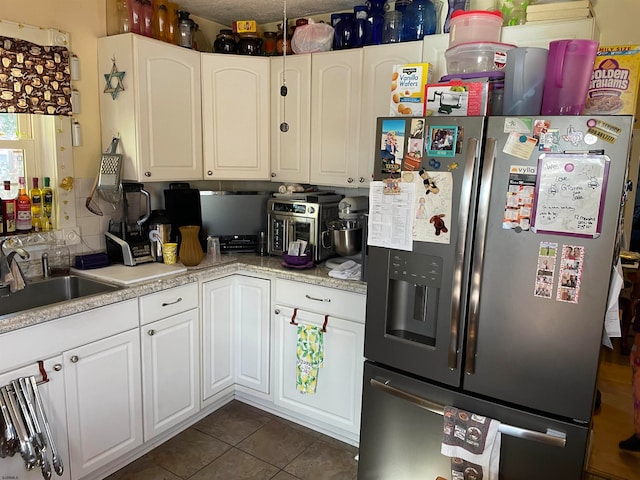 kitchen featuring stainless steel fridge, white cabinetry, sink, and dark tile patterned floors