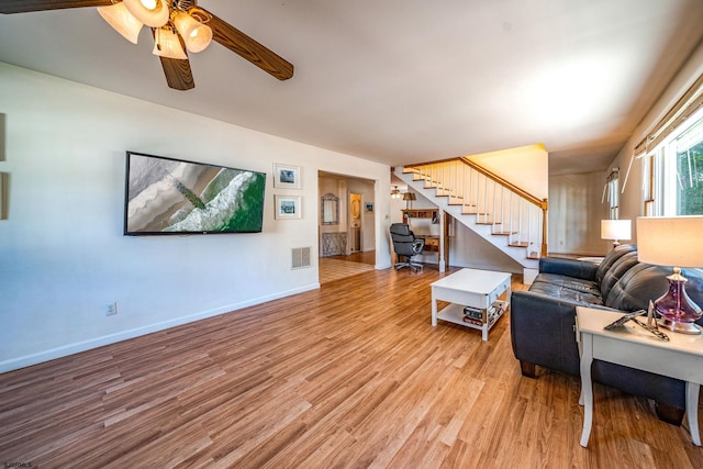 living room with visible vents, stairway, light wood-style floors, a ceiling fan, and baseboards