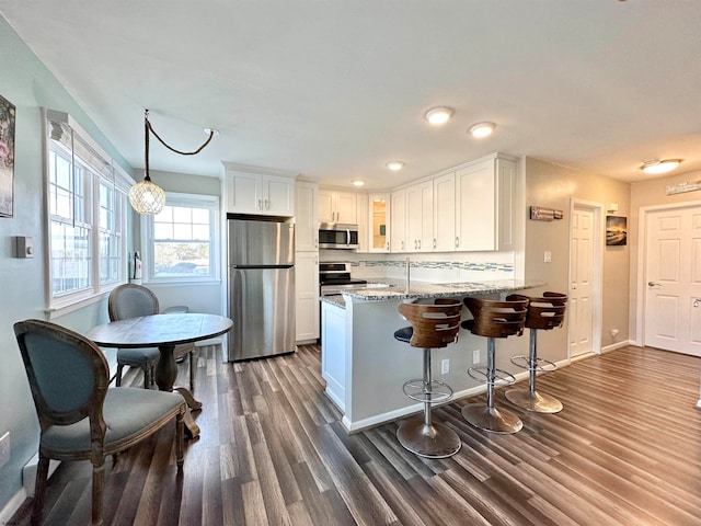 kitchen with white cabinetry, kitchen peninsula, light stone counters, appliances with stainless steel finishes, and dark hardwood / wood-style floors