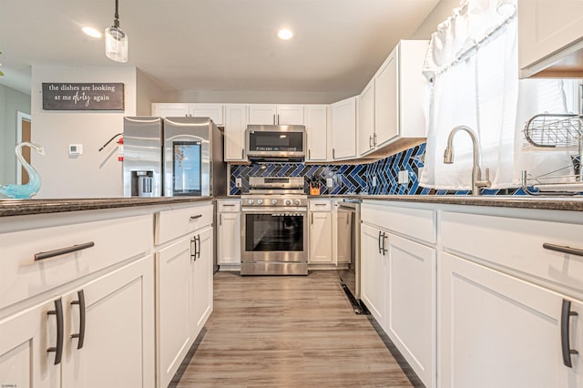 kitchen with white cabinets, hanging light fixtures, tasteful backsplash, light wood-type flooring, and appliances with stainless steel finishes