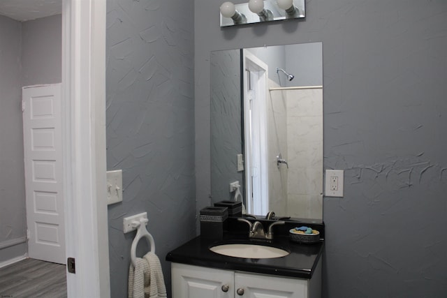 bathroom with hardwood / wood-style flooring, vanity, and a tile shower