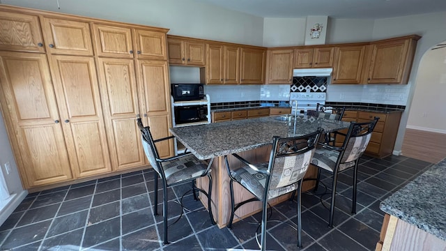 kitchen featuring a kitchen bar, black appliances, a center island with sink, and tasteful backsplash