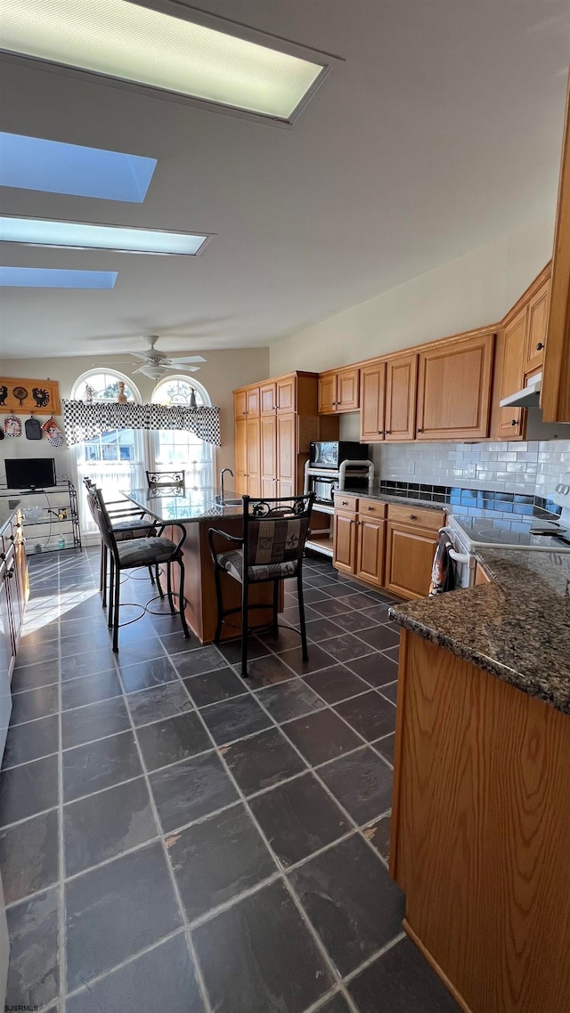 kitchen featuring ceiling fan, dark stone countertops, decorative backsplash, and a skylight