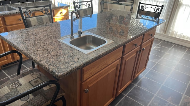 kitchen featuring dark stone counters, sink, a kitchen breakfast bar, and a kitchen island with sink