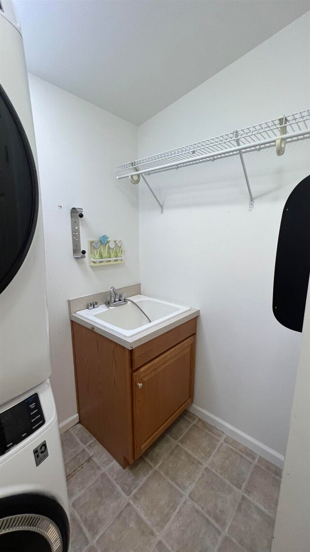 washroom featuring stacked washer and clothes dryer, cabinets, sink, and light tile patterned floors