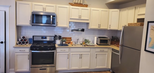 kitchen with stainless steel appliances, white cabinets, sink, and backsplash