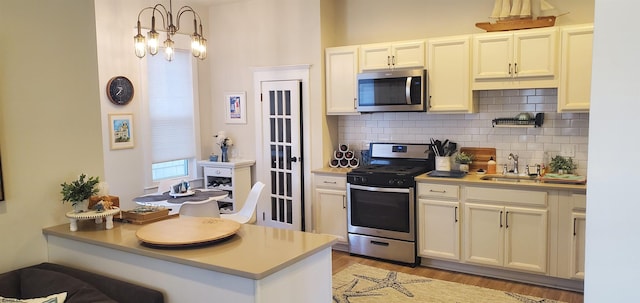 kitchen with light hardwood / wood-style flooring, hanging light fixtures, sink, a chandelier, and appliances with stainless steel finishes