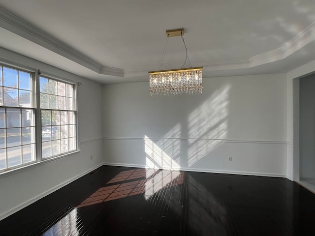 empty room with a tray ceiling, hardwood / wood-style floors, a notable chandelier, and crown molding