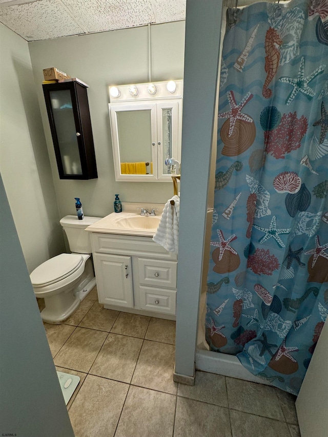 bathroom with a drop ceiling, toilet, tile patterned flooring, curtained shower, and vanity