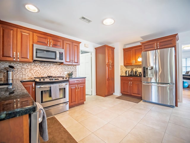 kitchen featuring decorative backsplash, stainless steel appliances, light tile patterned floors, and dark stone countertops