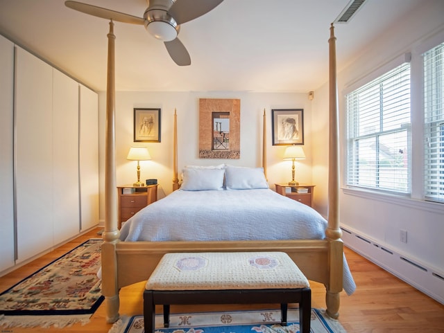 bedroom featuring a baseboard heating unit, light hardwood / wood-style floors, ceiling fan, and a closet