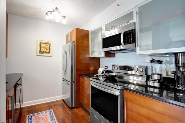 kitchen featuring stainless steel appliances, dark stone countertops, a textured ceiling, dark hardwood / wood-style flooring, and decorative backsplash