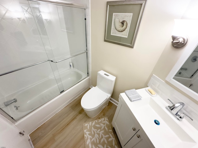 full bathroom with bath / shower combo with glass door, wood-type flooring, toilet, and vanity