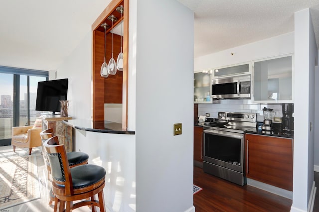 kitchen with backsplash, appliances with stainless steel finishes, a textured ceiling, a kitchen bar, and dark hardwood / wood-style flooring