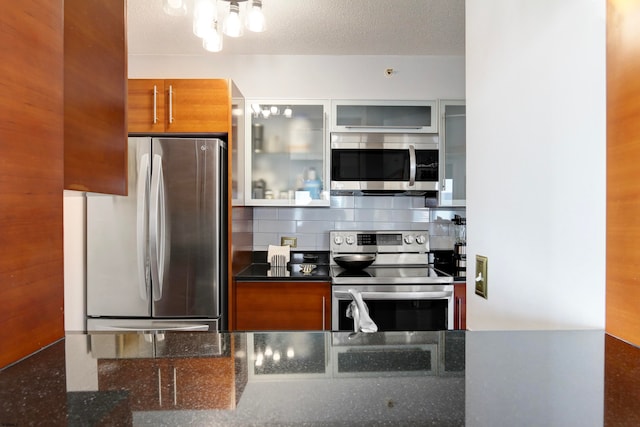 kitchen with dark stone countertops, a textured ceiling, appliances with stainless steel finishes, and tasteful backsplash