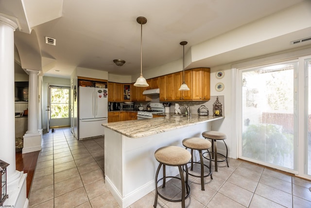 kitchen featuring pendant lighting, light tile patterned floors, white appliances, kitchen peninsula, and decorative columns