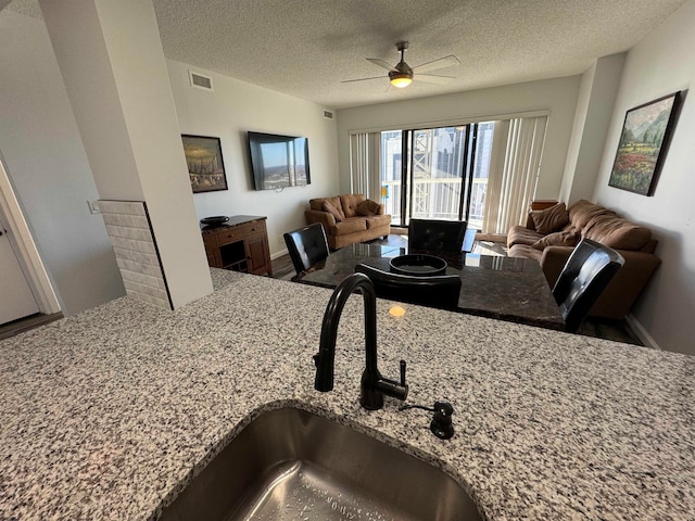 kitchen with ceiling fan, a textured ceiling, light stone counters, and sink