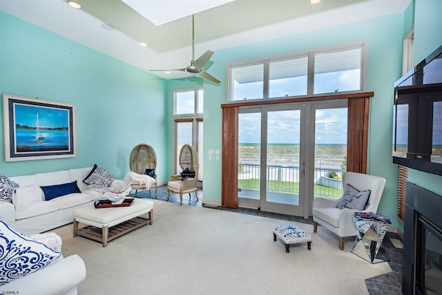 carpeted living room featuring a high ceiling, a skylight, and ceiling fan