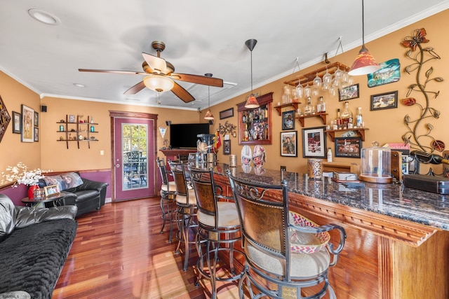 bar featuring hanging light fixtures, wood-type flooring, ceiling fan, and ornamental molding