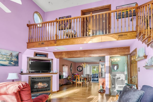 living room featuring a high ceiling, beam ceiling, light hardwood / wood-style floors, and ceiling fan with notable chandelier