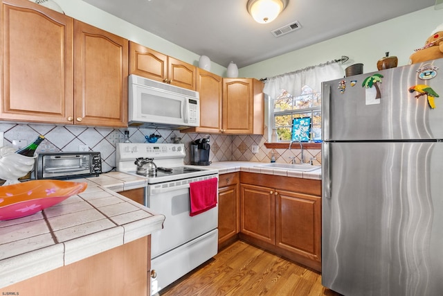 kitchen featuring sink, tasteful backsplash, white appliances, tile counters, and light wood-type flooring