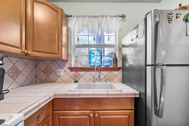 kitchen with tile counters, decorative backsplash, sink, and stainless steel refrigerator