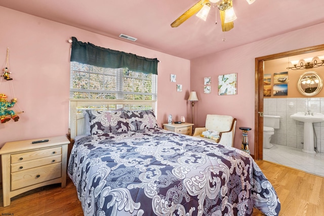 bedroom with tile walls, hardwood / wood-style floors, ceiling fan, and ensuite bathroom