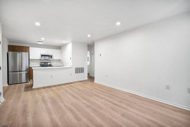 kitchen with kitchen peninsula, white cabinetry, appliances with stainless steel finishes, and light wood-type flooring