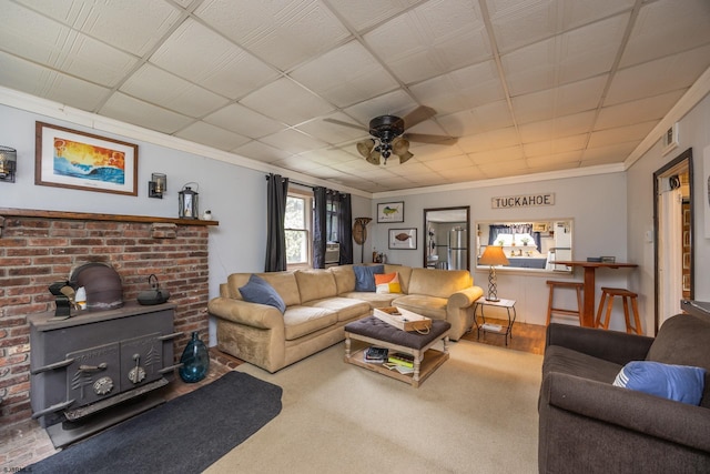 living room with ornamental molding, carpet, ceiling fan, and a wood stove