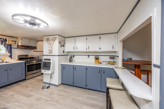 kitchen featuring heating unit, backsplash, stainless steel gas range oven, and blue cabinetry