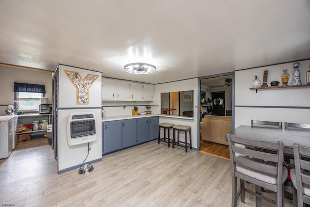 kitchen featuring heating unit, washer / dryer, white cabinets, and light wood-type flooring