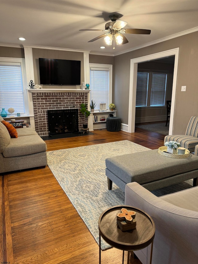 living room featuring hardwood / wood-style floors, ceiling fan, ornamental molding, and a brick fireplace