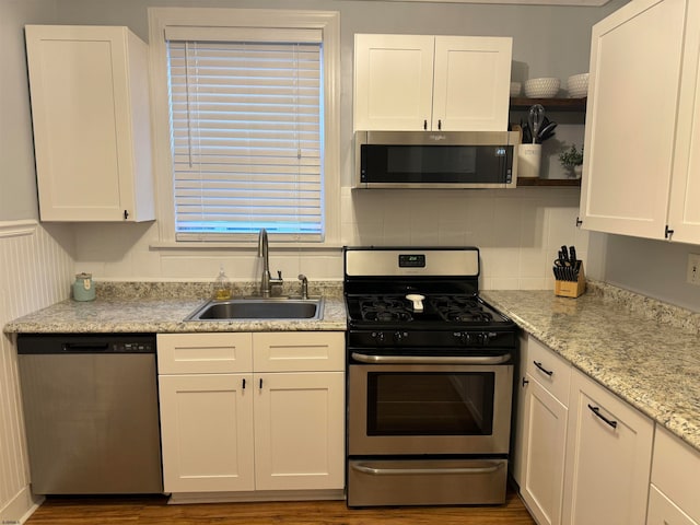 kitchen with light stone countertops, white cabinetry, sink, stainless steel appliances, and wood-type flooring